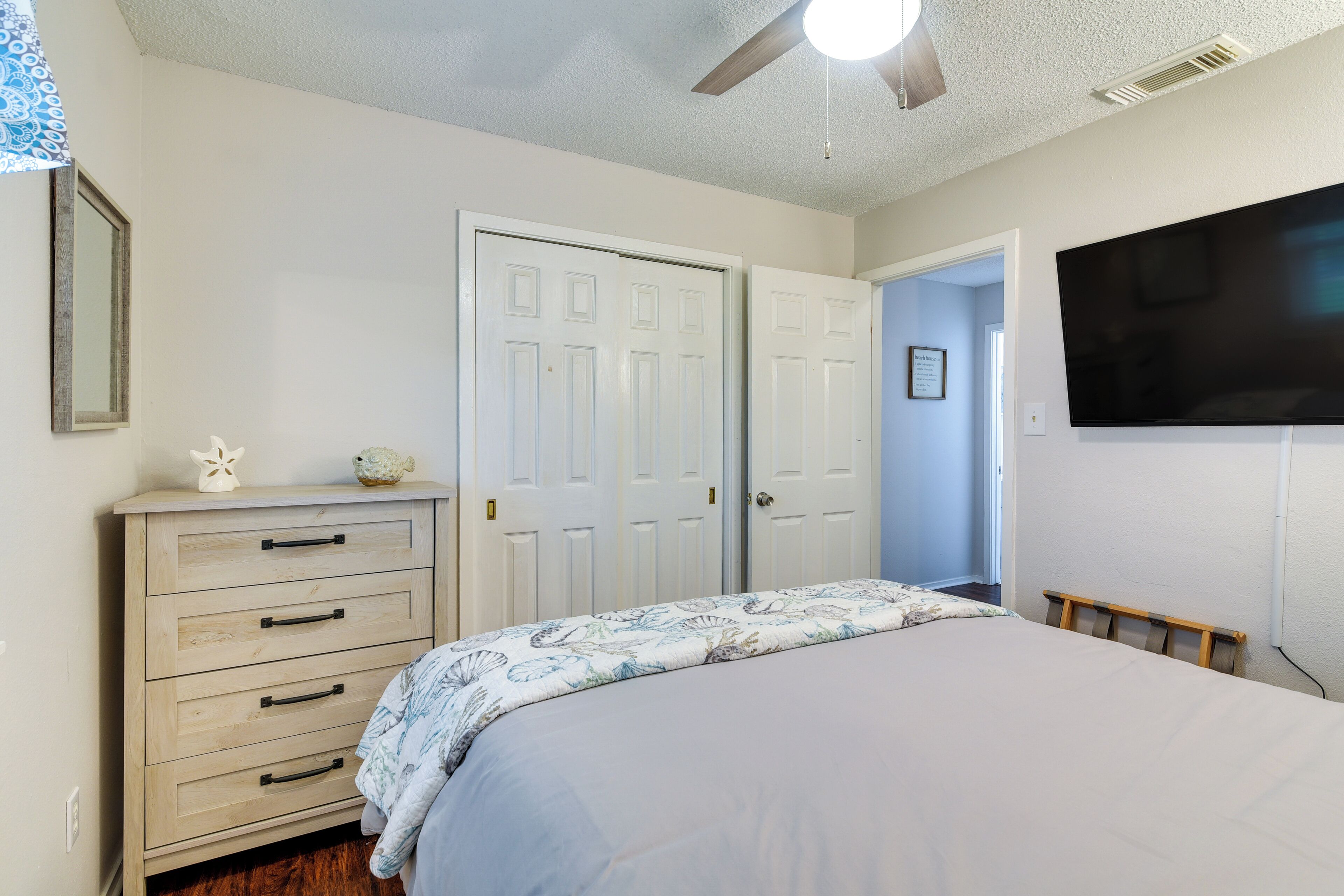 A bedroom with a bed, a dresser, a ceiling fan, and a TV mounted on the wall.