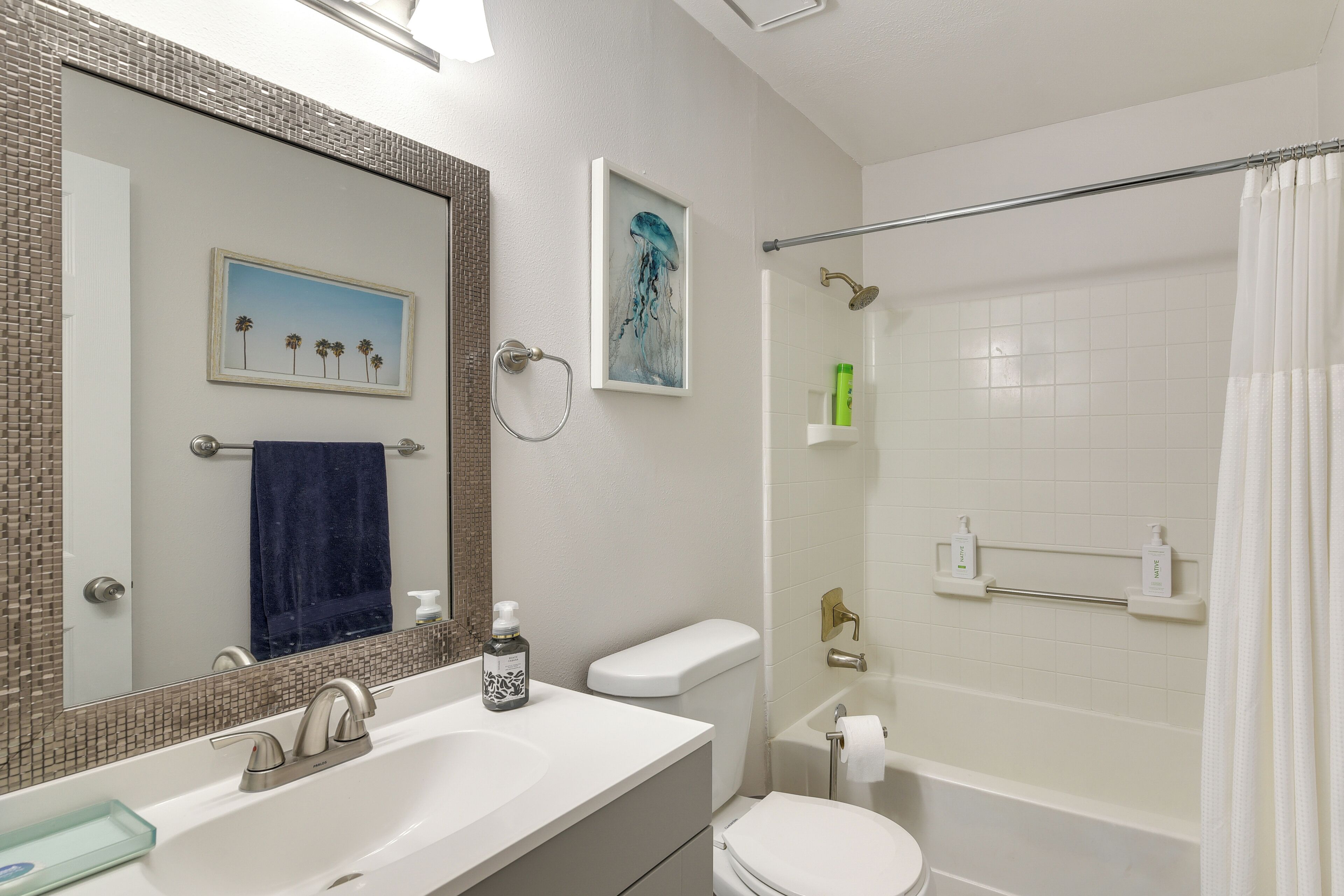 A bathroom with a white sink, a toilet, a shower with a glass door, and a mirror with a mosaic backsplash.
