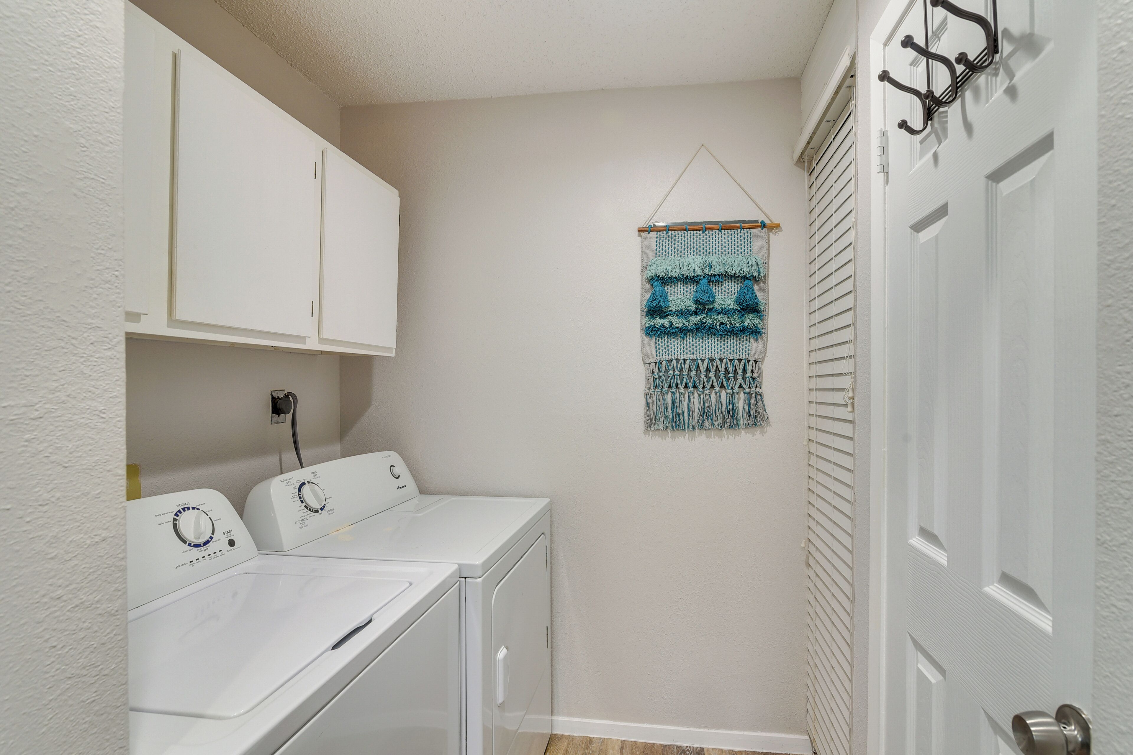 A laundry room with white cabinets, a washing machine, and a drying rack.