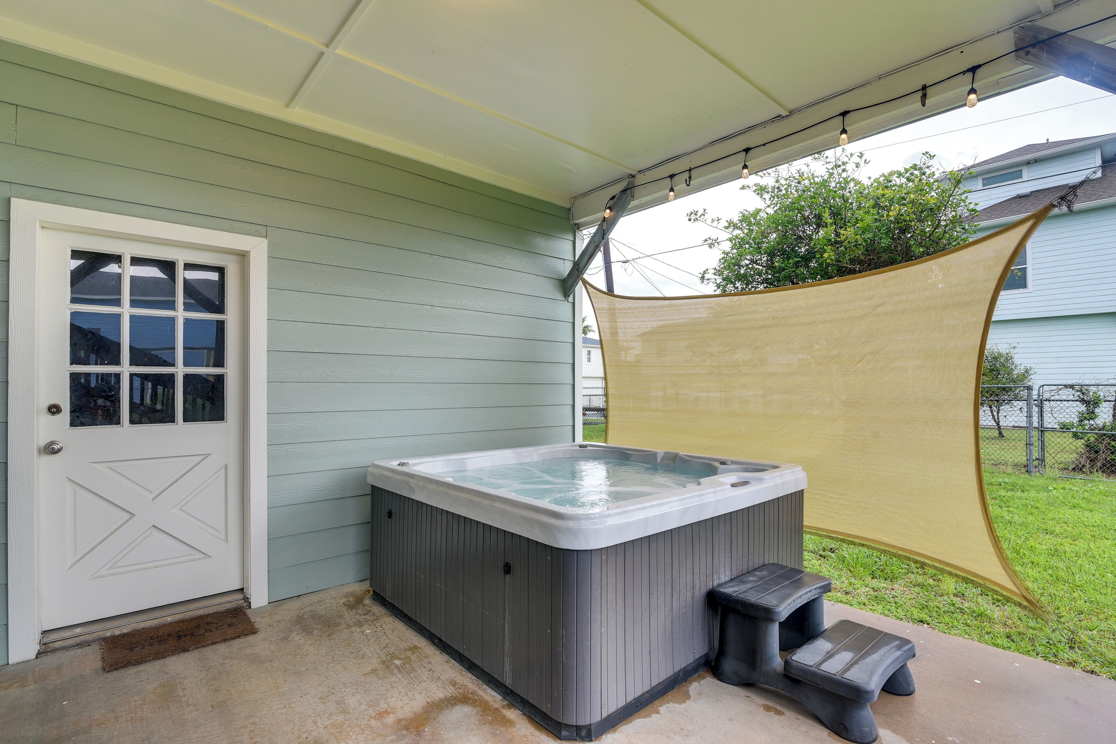 A hot tub outside a house with a door and a covered patio area.