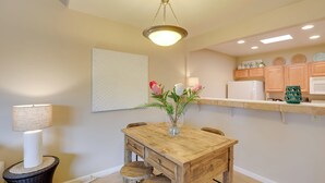 A dining area with a wooden table, chairs, a vase with flowers, a lamp, and a hanging light fixture.