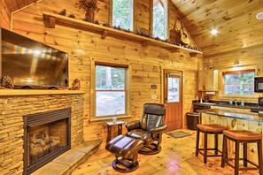 A cozy cabin interior with a stone fireplace, leather recliner, wooden shelves, and a kitchen area. - Charming Murphy Cabin w/ Porch - Near Hiking! (Murphy)