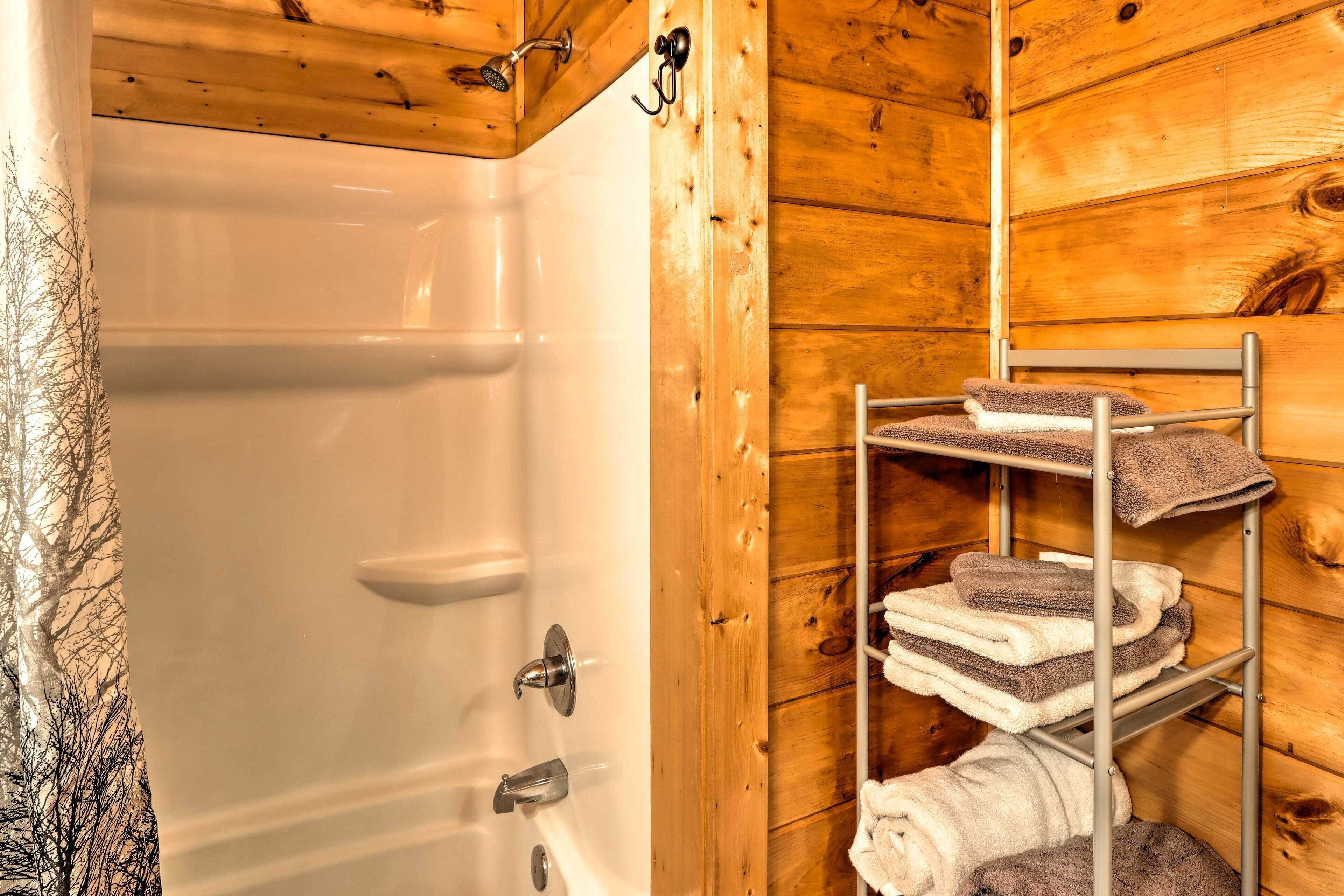 Une salle de bain rustique, avec des murs en bois, une baignoire blanche, un porte-serviettes en métal sur lequel sont pliées des serviettes, et un plafond en bois.