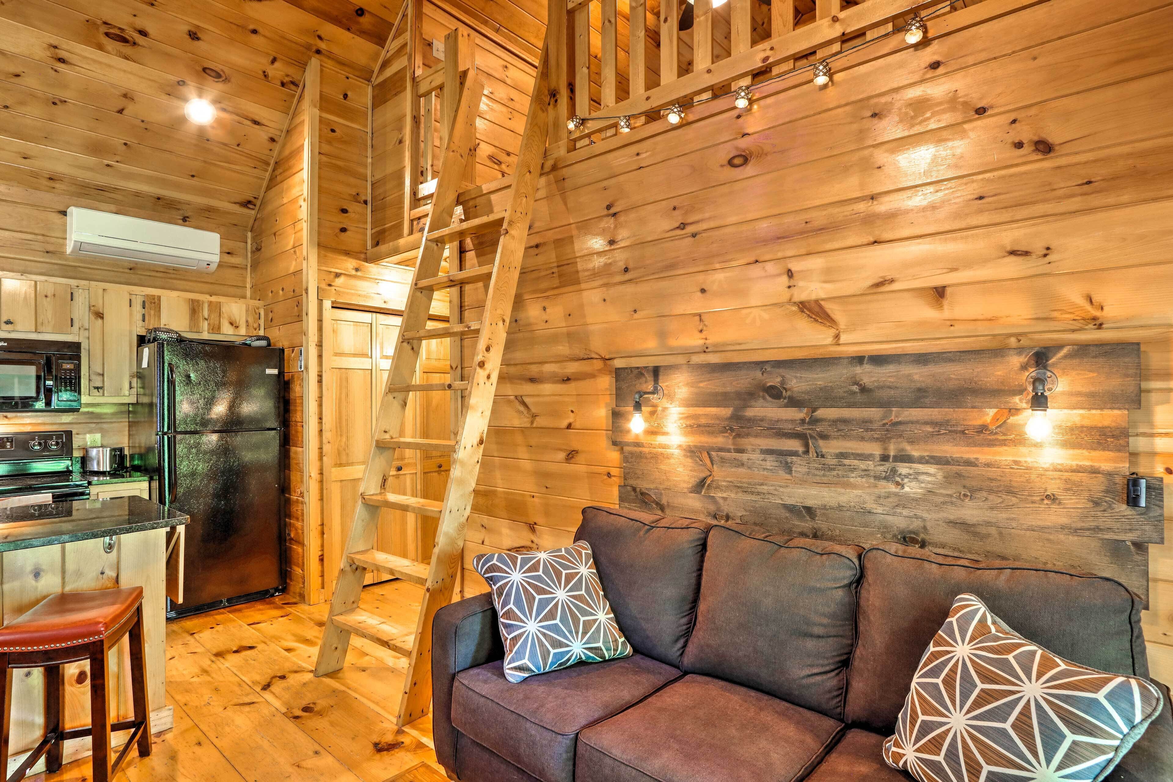 L’intérieur d’un chalet en bois comprend une cuisine, un canapé agrémenté de coussins à motifs et une échelle en bois.