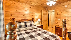 Un dormitori de cabana de fusta amb un llit, sivelles, una làmpada, un ventilador de sostre i una porta de fusta.