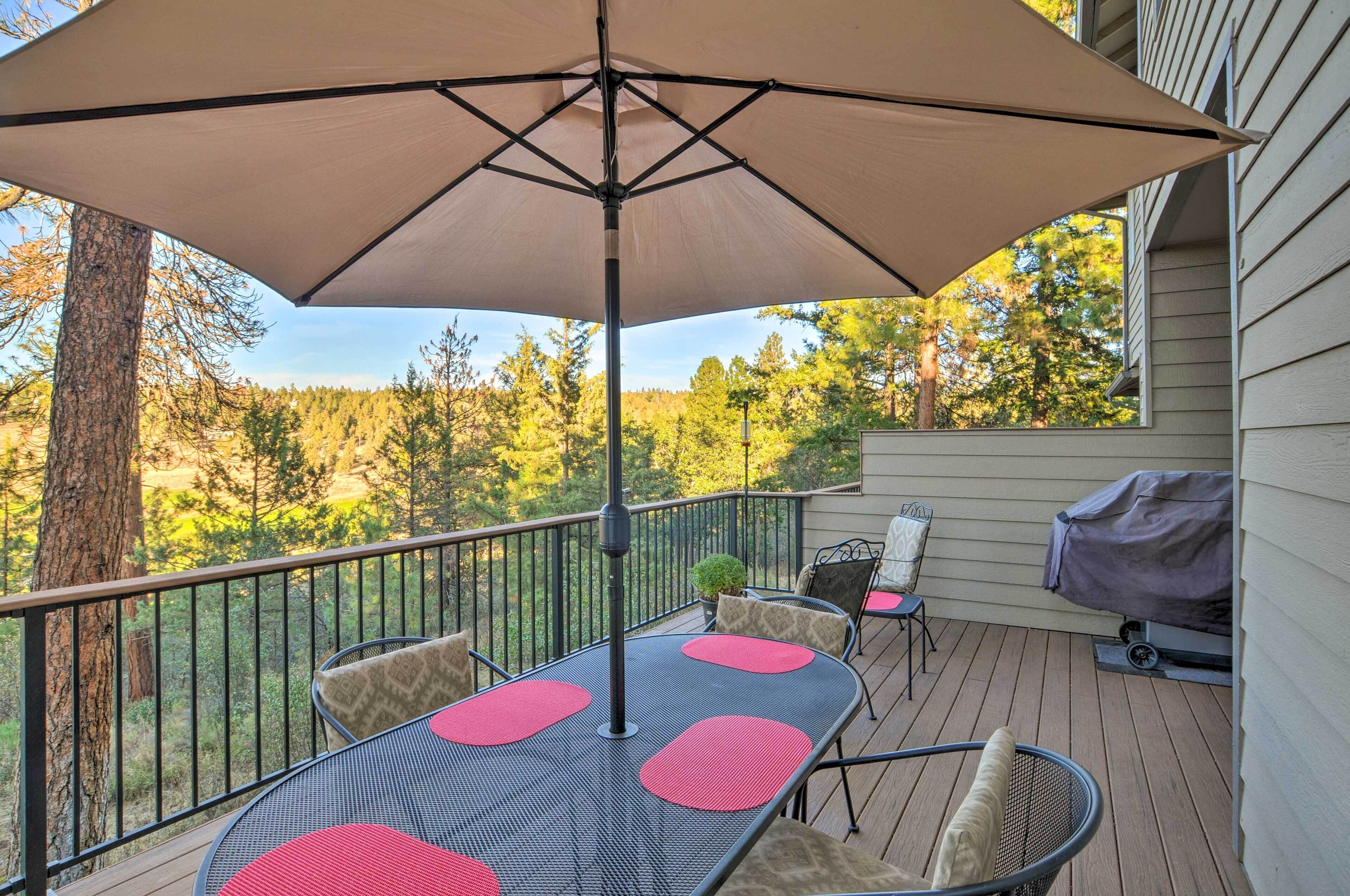 Une terrasse avec une table et des chaises, un barbecue et une vue sur les arbres.