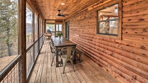 A wooden cabin with a dining area featuring a table and chairs, large windows, and a ceiling fan. - Piney Bluff Retreat With Mountain Views! (Melbourne)