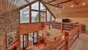 A spacious cabin with a stone wall, large windows, a wooden deck, and a cozy seating area. - Piney Bluff Retreat With Mountain Views! (Melbourne)