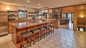 A spacious kitchen with a large island, wooden bar stools, and a stone fireplace. - Piney Bluff Retreat With Mountain Views! (Melbourne)
