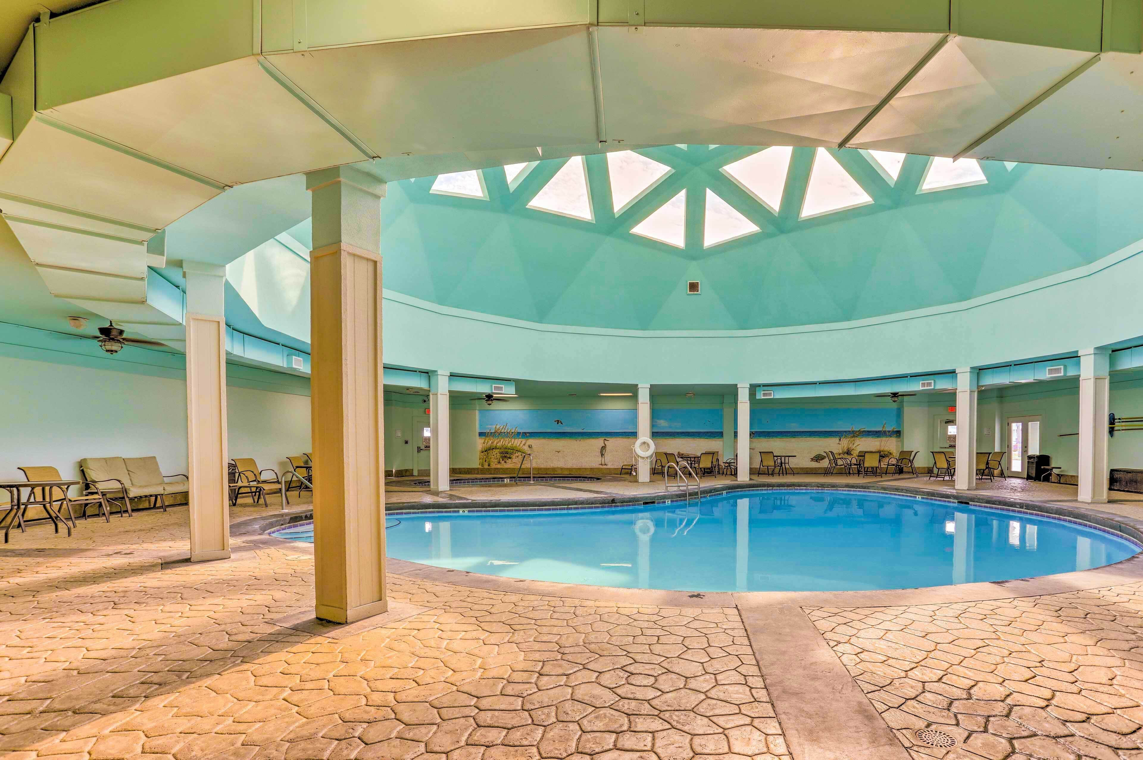 An indoor swimming pool with a skylight ceiling, lounge chairs, and a tiled floor.