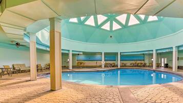 An indoor swimming pool with a skylight ceiling, lounge chairs, and a tiled floor.