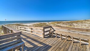 A wooden boardwalk leading to a beach with a flag in the distance. - Resort Perks: Gulf Shores Beach-inspired Condo! (Gulf Shores)