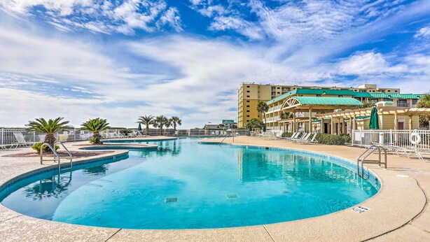 A large outdoor swimming pool with a clear blue sky and a multi-story building in the background. - Resort Perks: Gulf Shores Beach-inspired Condo! (Gulf Shores)