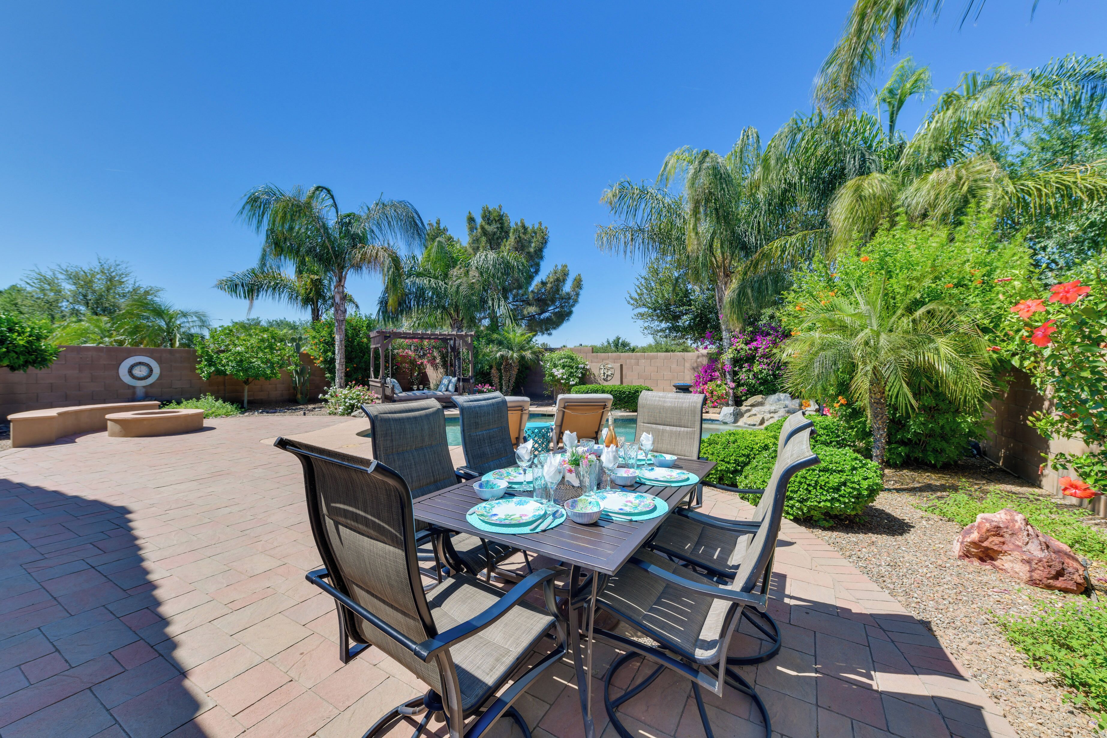 An outdoor patio with a table set for dining, surrounded by chairs and a pool in the background.