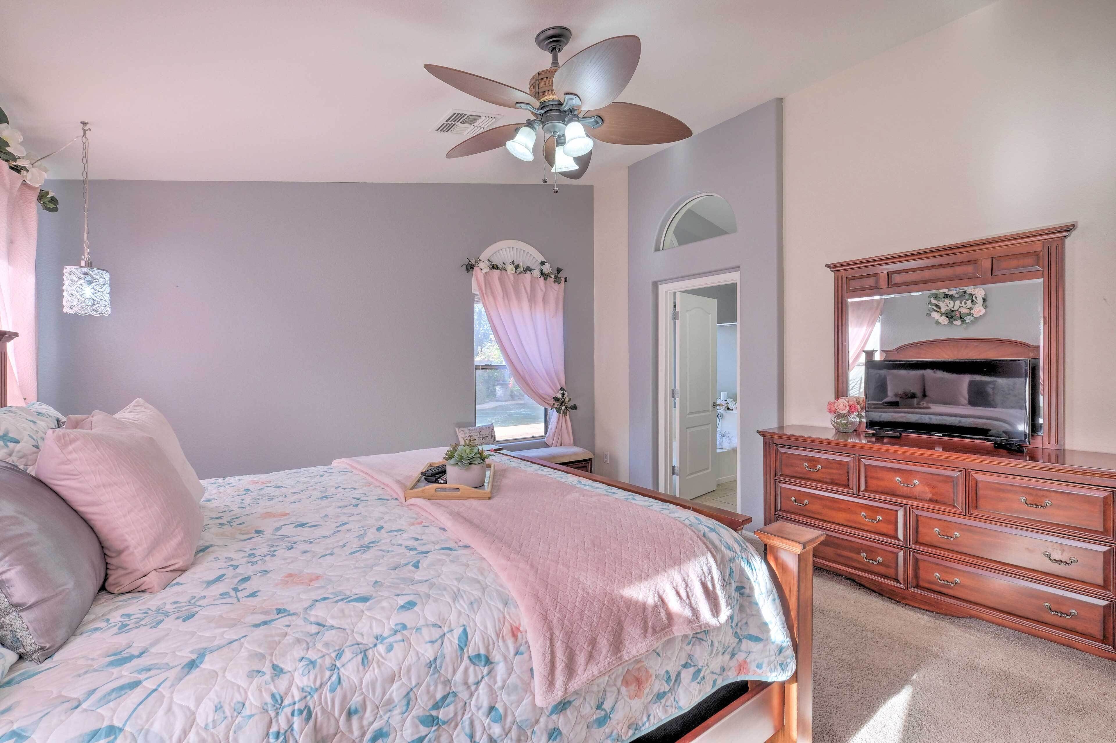 A bedroom with a bed, a dresser, a ceiling fan, a window with curtains, and a mirror.