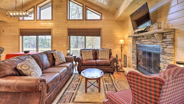 A cozy cabin interior with a stone fireplace, leather sofas, and a large window overlooking a forest. - Chestertown Hideaway w/ Lake & Beach Access! (Chestertown)