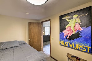 Quarto com cama, um cartaz na parede e porta que dá para outro espaço.