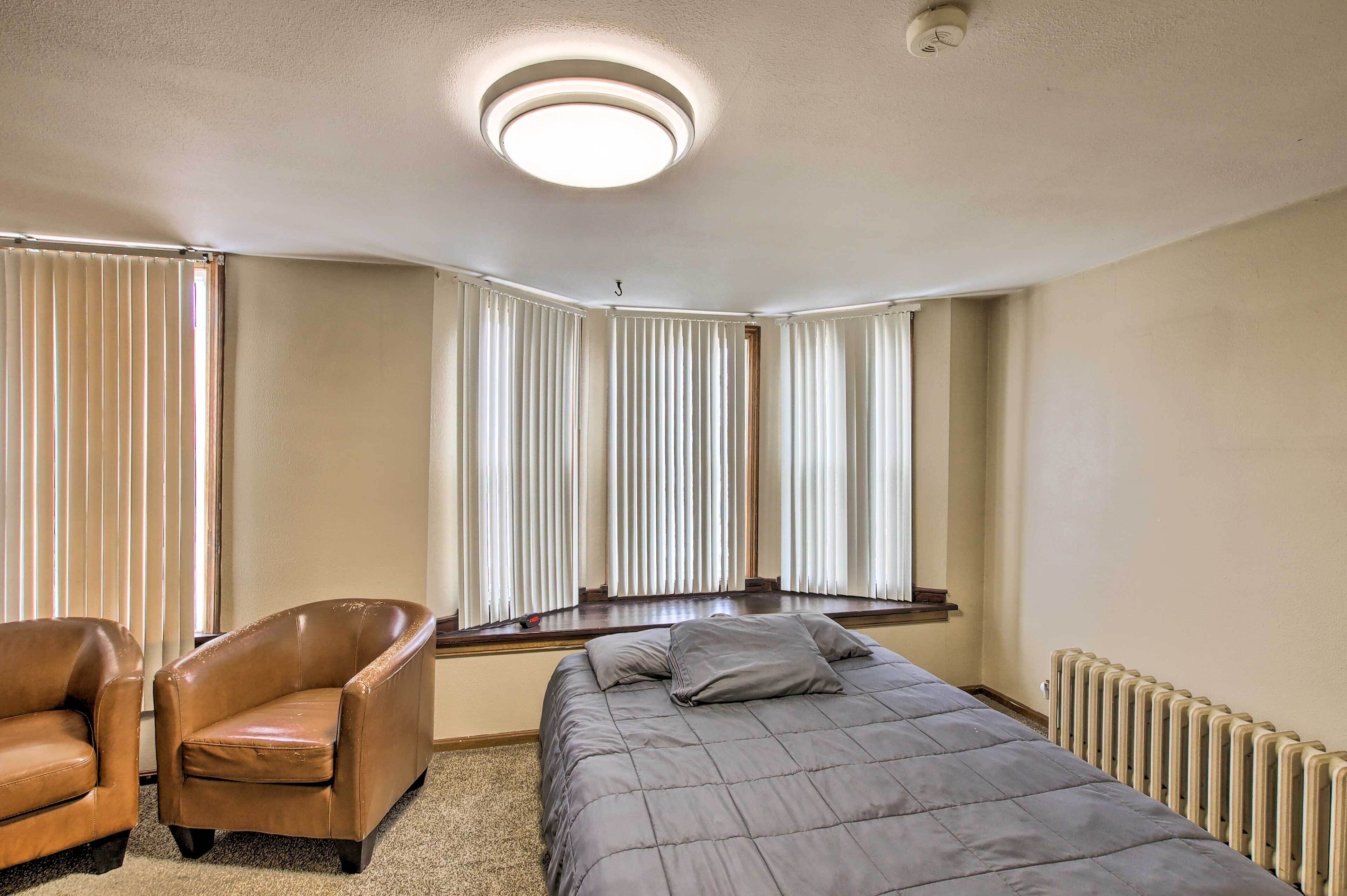 A bedroom with a bed, a chair, and a window with blinds.