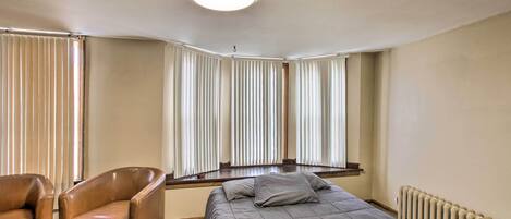 A bedroom with a bed, a chair, and a window with blinds.