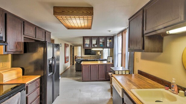 A compact kitchen with dark wooden cabinets, a black refrigerator, a wooden countertop, and a sink with a mirror above it.