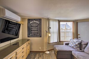 Un salón acogedor con un televisor de pantalla plana, un mueble de madera, un sofá con un cojín estampado y un cartel de whisky Jack Daniel's en la pared.