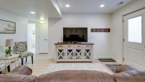 A living room with a television, a cabinet, a sofa, and a door. - Orem Vacation Rental w/ Shared Yard & Hot Tub (Orem)