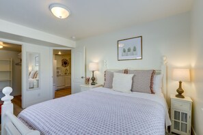 A neatly arranged bedroom with a large bed, bedside lamps, a framed picture on the wall, and a small cabinet.