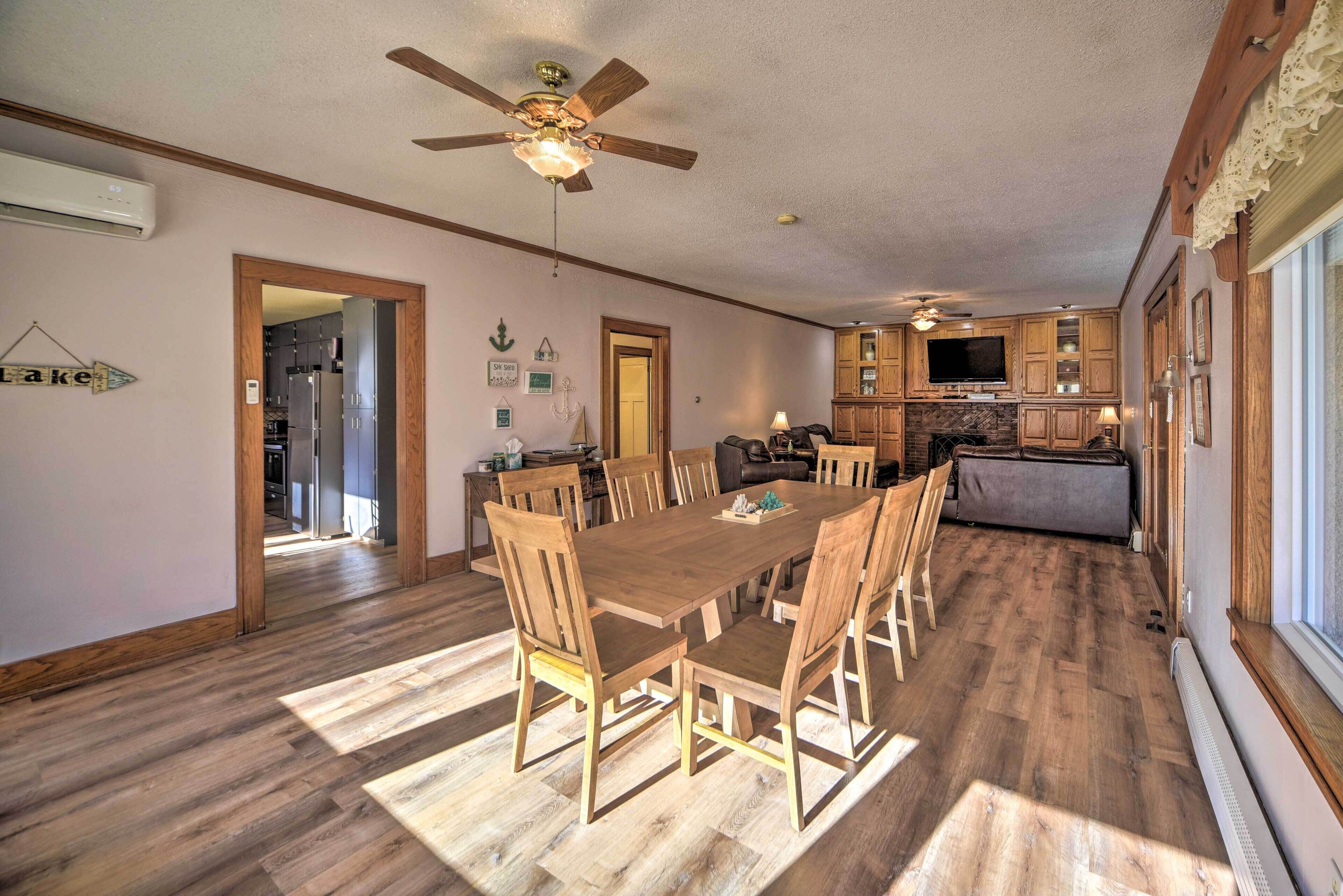 Un grand espace à manger avec une table et des chaises en bois, un ventilateur de plafond et une cuisine en arrière-plan.
