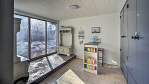 Una habitación con un ventanal grande, un banco de madera, un estante con objetos coloridos y un armario gris.