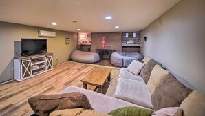 Una sala de estar con piso de madera, un sofá, una mesa de centro, un televisor sobre un mueble blanco y una pared de ladrillo decorativa.
