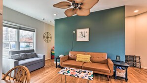 Ein Wohnzimmer mit braunem Ledersofa, einem grauen Sofa, einem Holzstuhl, einem Couchtisch, einem Deckenventilator und einem Fenster mit Jalousien.