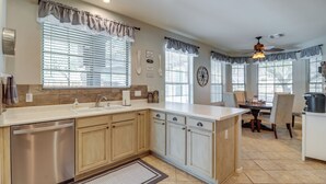 Una cocina moderna con lavavajillas, armarios de madera, una zona de comedor con mesa y sillas, y un ventilador de techo.