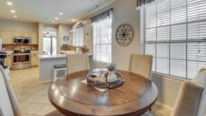 Una cocina moderna con electrodomésticos integrados, un comedor con mesa redonda y un amplio ventanal con persianas.