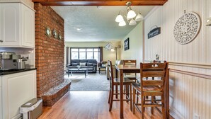 A kitchen with a brick wall, wooden ceiling beams, and a dining area with wooden chairs and a table. - Cozy Lewiston Home < 10 Mi to Niagara Falls! (Lewiston)