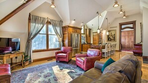 A spacious living room with a high ceiling, wooden beams, a large sofa, a television, and a dining area with chairs and a table. - Historic Guest House on Castle Kimble Estate! (Manhattan)