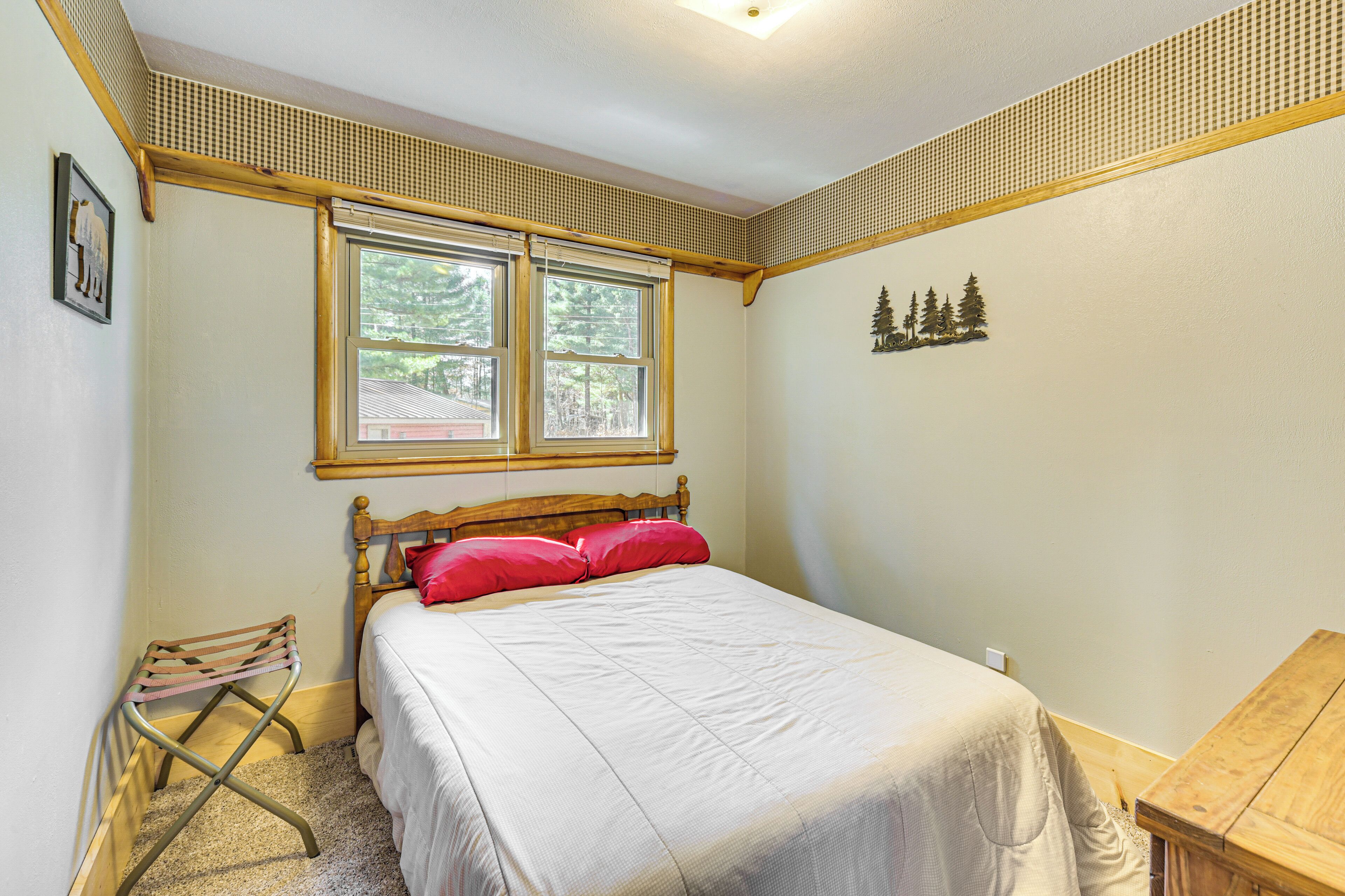 Un dormitorio con una cama, una ventana, una mesita de madera y un cuadro en la pared.