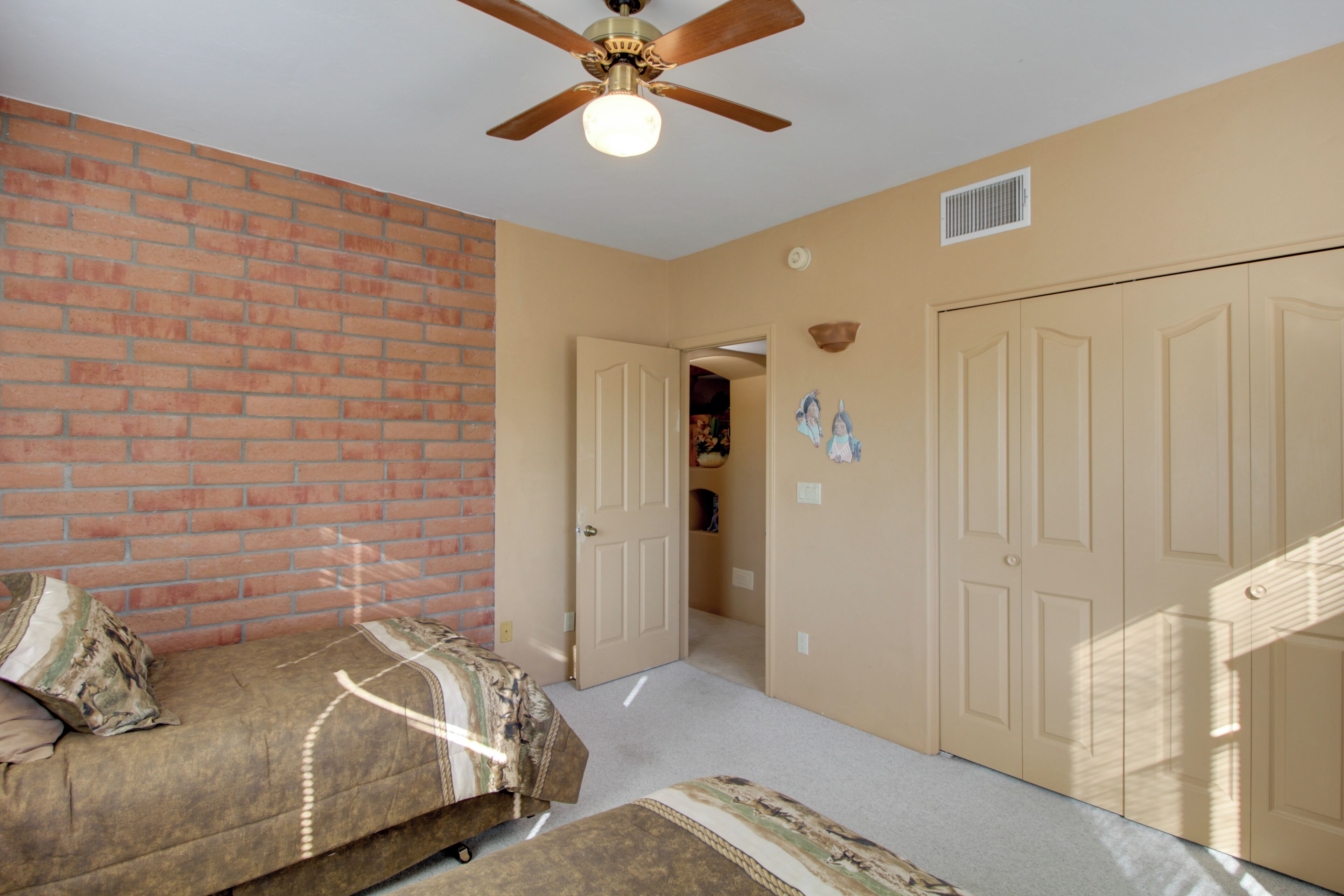A room with a brick wall, a ceiling fan, a door leading to another room, and a closet with doors.