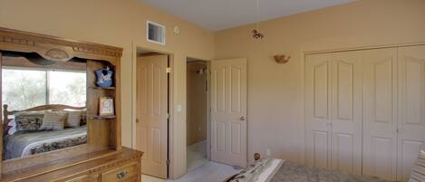 A bedroom with a wooden dresser, a large bed, a ceiling fan, and a door leading to another room.