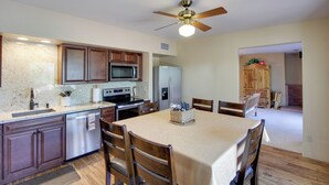 A modern kitchen with wooden cabinets, stainless steel appliances, and a dining area with a table and chairs. - Tucson Home - Hiking Trail Access On-site! (Tucson)