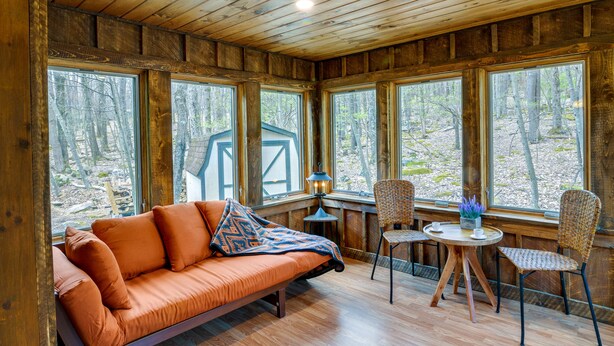 A cozy cabin interior with a wooden ceiling, large windows, a sofa, a table, and chairs. - Alpine Lake Resort Cabin Rental w/ Pool Access! (Terra Alta)
