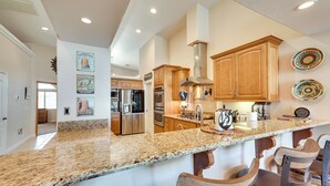 A kitchen with granite countertops, wooden cabinets, stainless steel appliances, and a bar area with bar stools. - Lake Havasu City Escape w/ Pool, Patio & Grill! (Lake Havasu City)