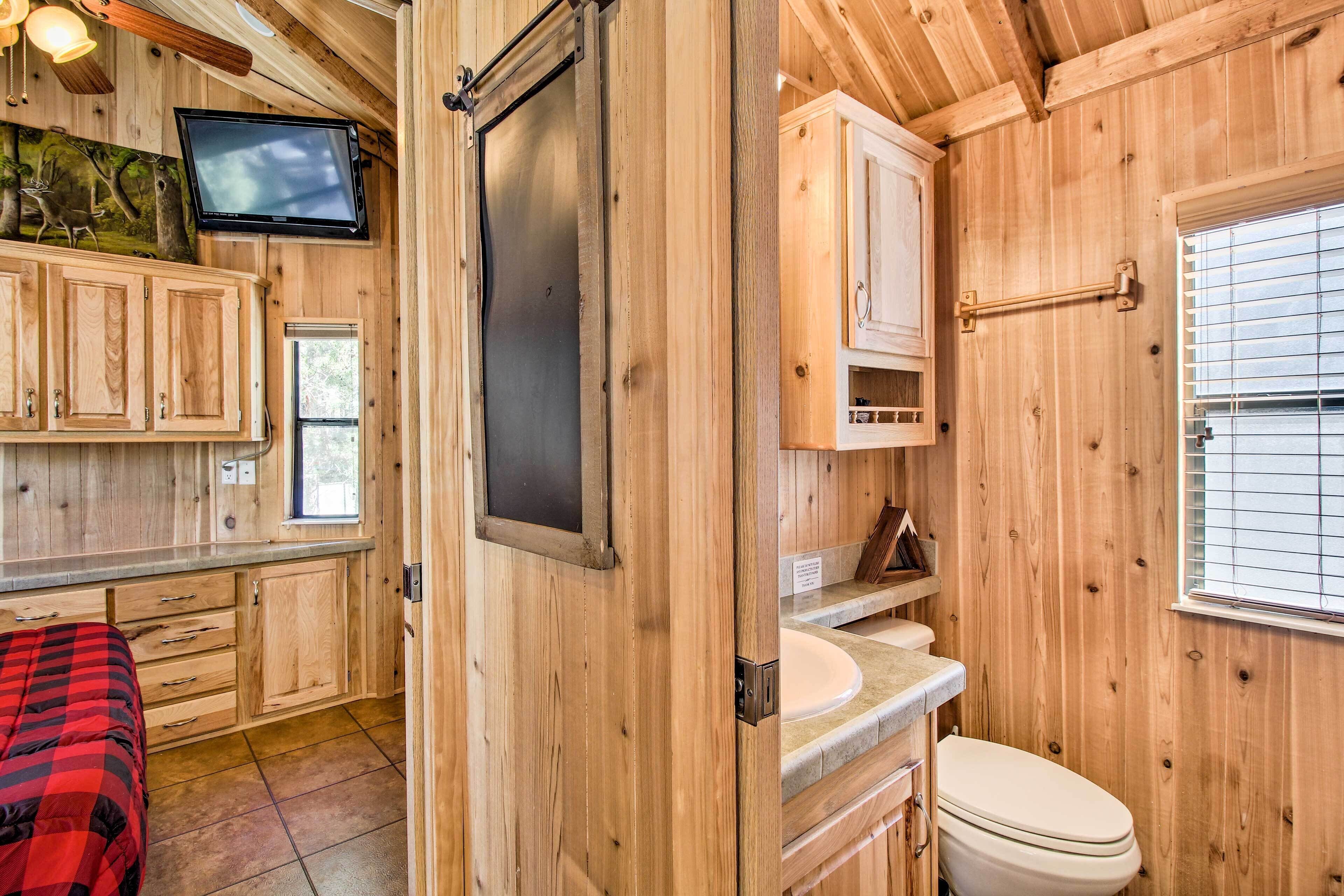 A wooden cabin interior with a bed, a television, cabinets, a sink, and a toilet.
