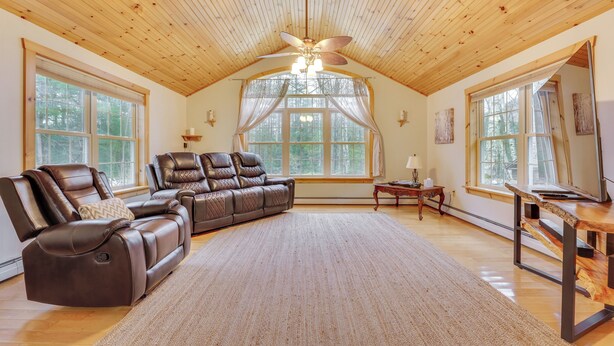 Un salon spacieux doté d’un grand canapé d’angle, d’un ventilateur de plafond et de grandes fenêtres laissant entrer la lumière naturelle.