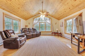 A spacious living room with a large sectional sofa, a ceiling fan, and large windows providing natural light. - Athol Vacation Rental w/ Mountain Views! (Athol)