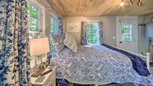 A bedroom with a large bed, a nightstand, a lamp, and a window with curtains. - Lush Edgecomb Studio Cottage w/ Fire Table! (Edgecomb)