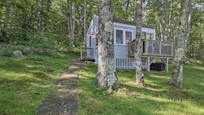 A cabin with a deck, surrounded by trees and a grassy area. - Lush Edgecomb Studio Cottage w/ Fire Table! (Edgecomb)