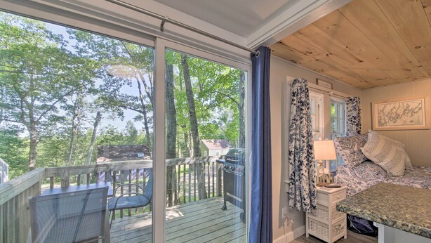 A bedroom with a large window, a wooden deck, and a view of trees. - Lush Edgecomb Studio Cottage w/ Fire Table! (Edgecomb)