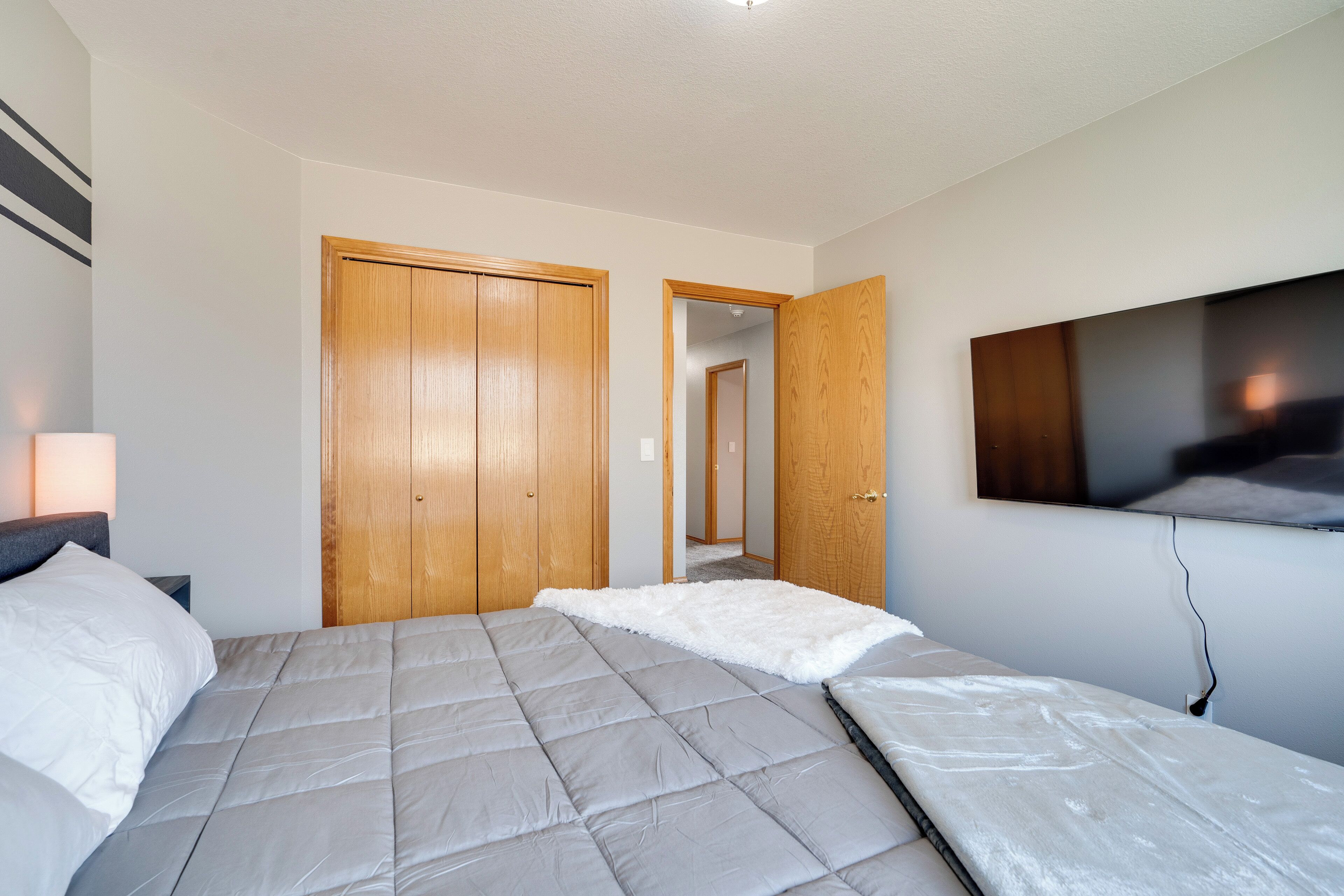 A bedroom with a bed, a TV mounted on the wall, and wooden doors.