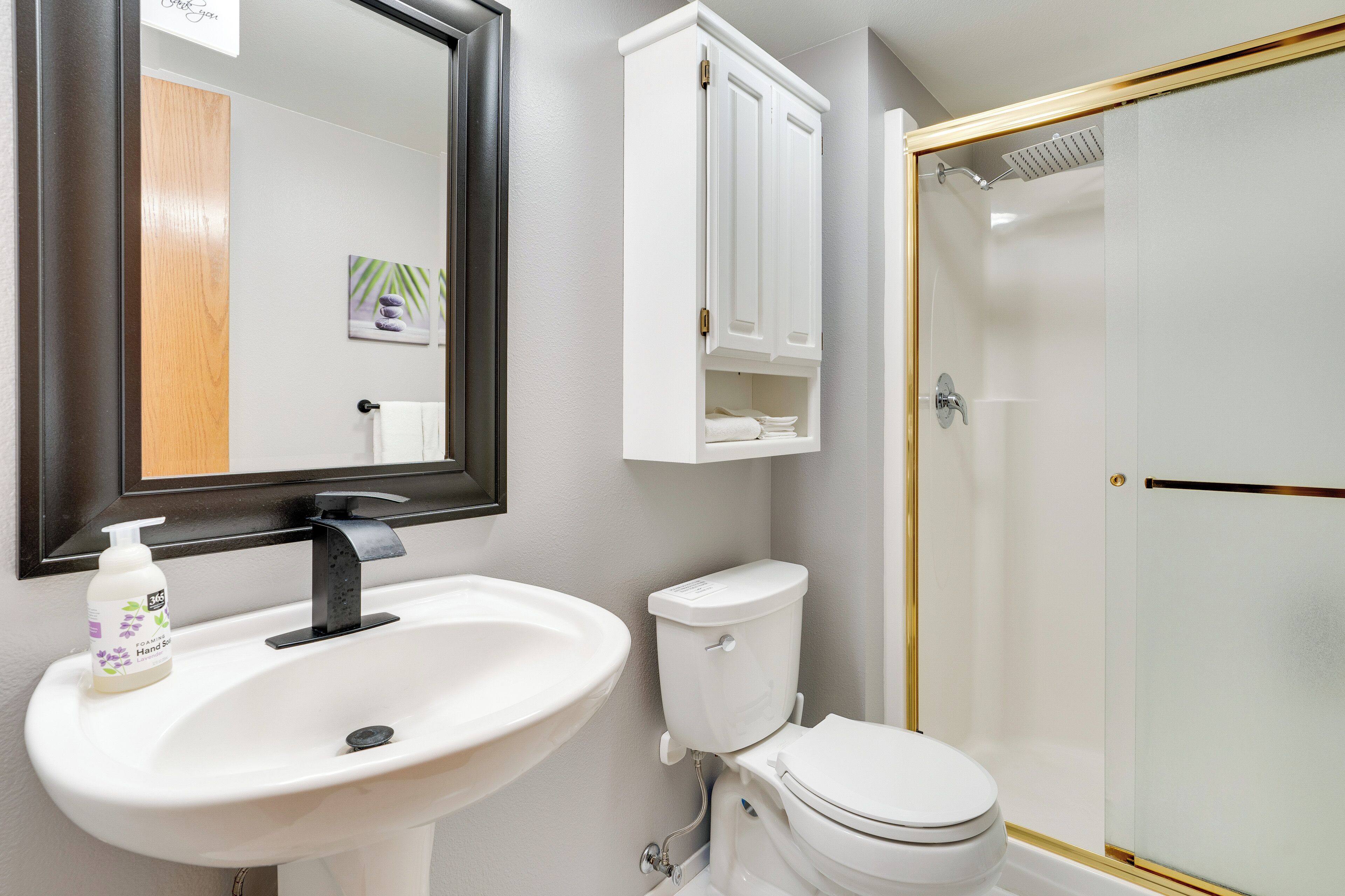 A bathroom with a white sink, a toilet, a mirror, and a shower enclosure.