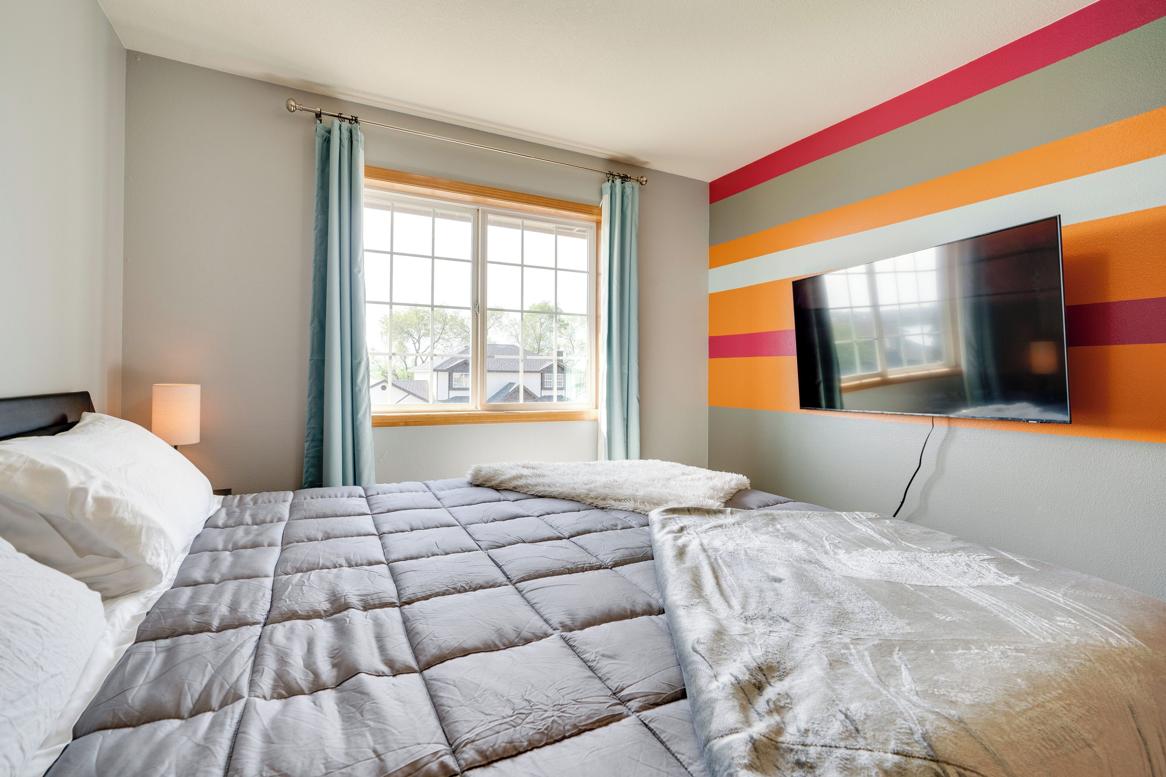 A hotel room with a bed, a TV mounted on the wall, and a window with curtains.